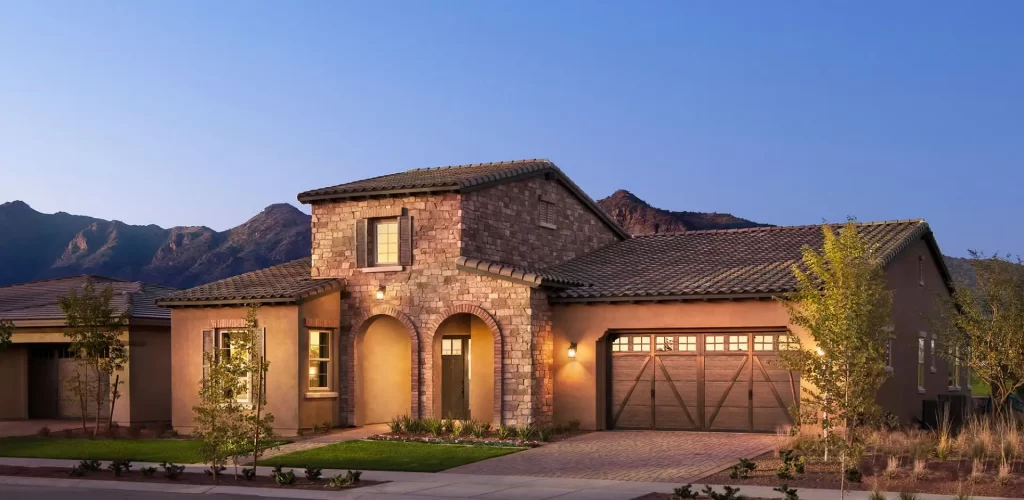 Modern stone house in a scenic setting, featuring a welcoming entrance, landscaped yard, and mountain backdrop, representing potential property value for homeowners and investors.