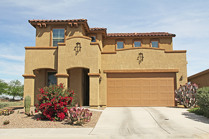 Desert-style home with stucco exterior, garage door, and landscaped front yard featuring cacti and flowering shrubs, relevant to Cactus Home Offer's property sales in Arizona.