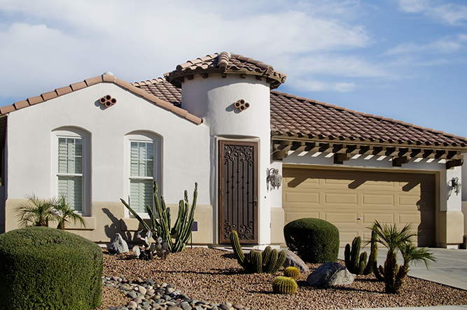 Arizona-style home with a tiled roof, decorative entryway, and desert landscaping featuring cacti and shrubs.
